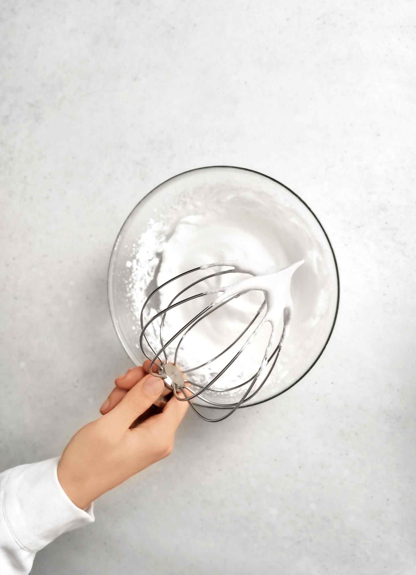 Hands whisking cream in a stainless bowl