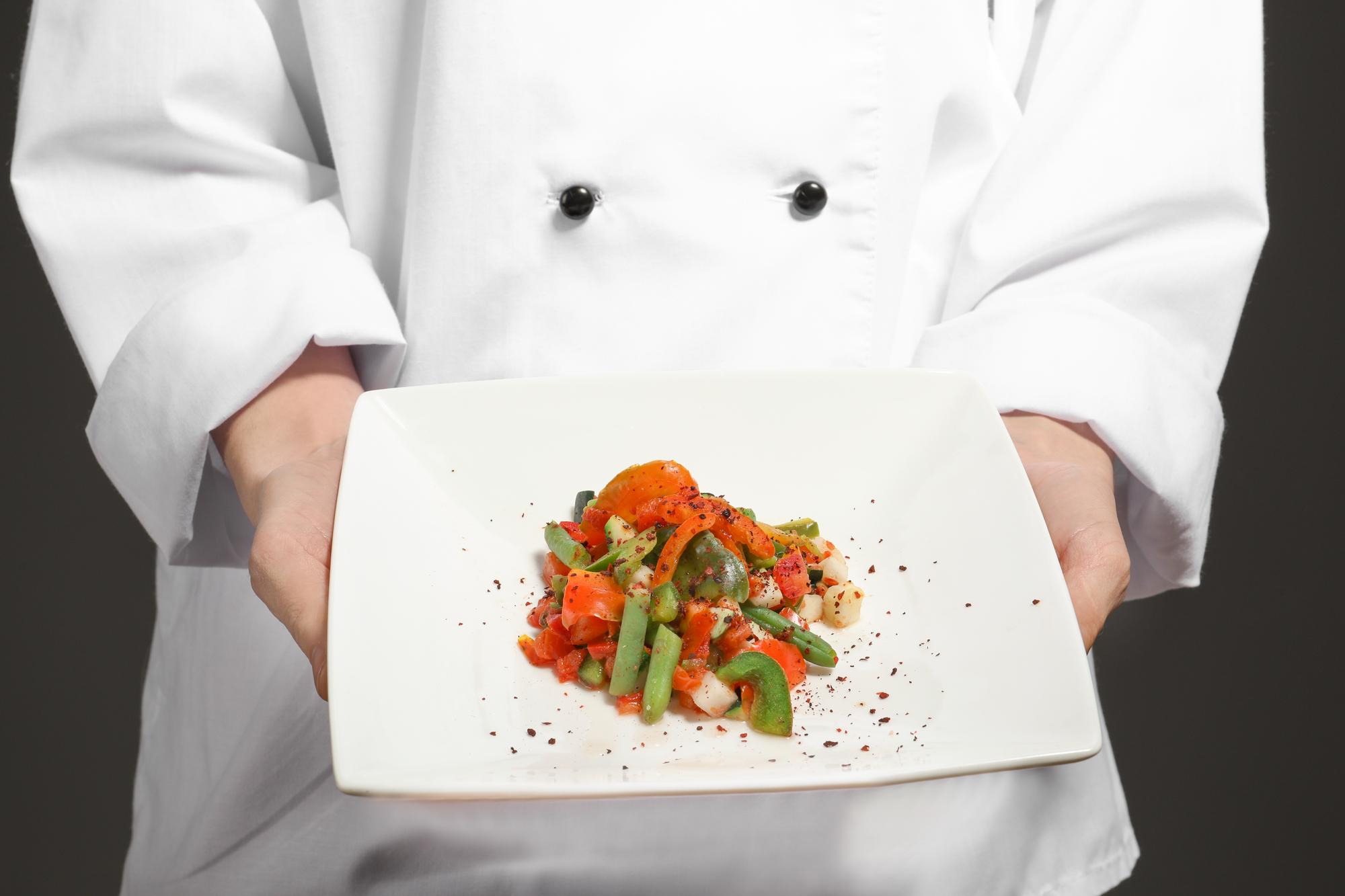Chef plating a contemporary dish on dark table